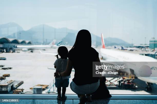 silhouette of young asian mother and cute little daughter looking at airplane through window at the airport while waiting for departure. family travel and vacation concept - baby gate imagens e fotografias de stock