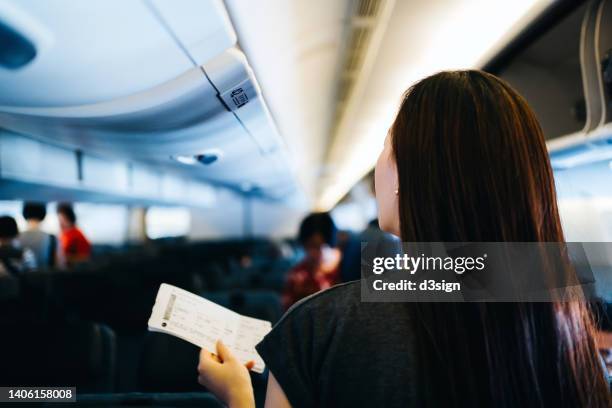 rear view of young asian female traveller holding her boarding pass, walking down the aisle in the airplane looking for her seat. travel and vacation concept - ekonomiklass bildbanksfoton och bilder