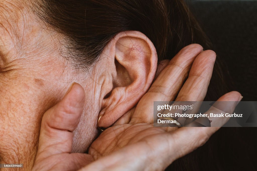A senior woman holding her ear, trying to hear