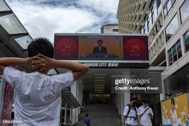 Pedestrians look at a screen showing live broadcast of Hong Kong Chief Executive John Lee speaking during a swearing-in ceremony for Hong Kong's new...
