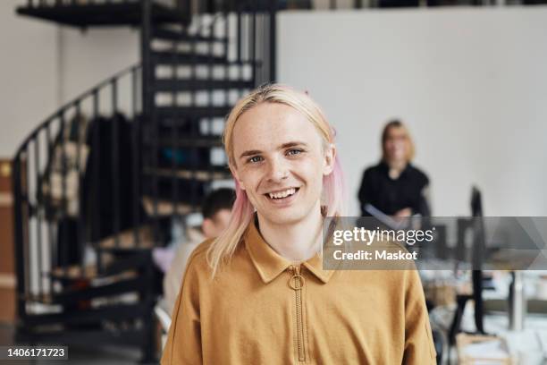 portrait of smiling non-binary computer programmer with dyed long hair at tech start-up office - transgender stockfoto's en -beelden