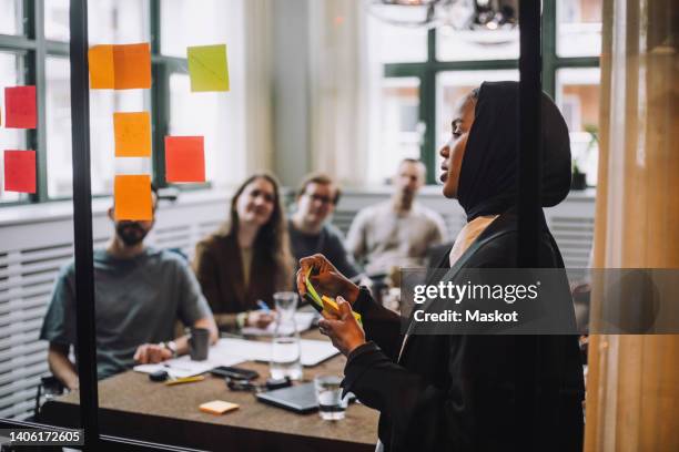 young woman with adhesive notes discussing plan with colleagues during meeting in creative office - veil stock pictures, royalty-free photos & images