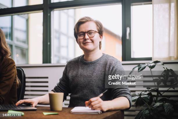 portrait of smiling young businessman wearing eyeglasses sitting with diary at conference table - ftm stock-fotos und bilder