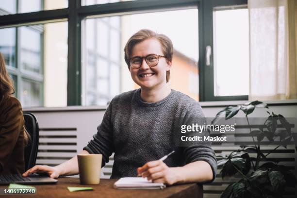 portrait of happy young male entrepreneur wearing eyeglasses while sitting at conference table - ftm stock-fotos und bilder