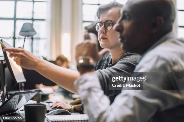 young businessman wearing eyeglasses discussing with male colleague while working in office - portrait of pensive young businessman wearing glasses stock-fotos und bilder