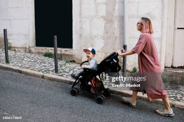 mother pushing son in baby stroller on street - the stroller stock pictures, royalty-free photos & images