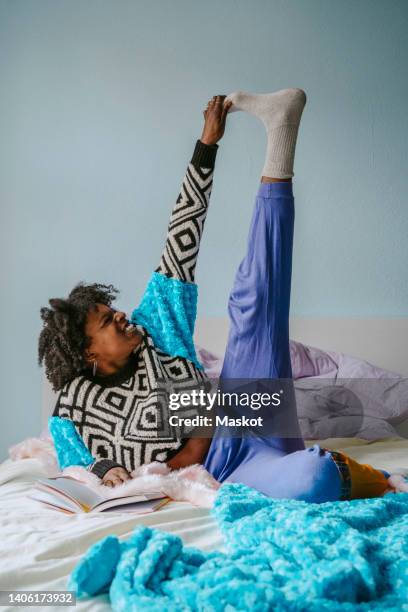happy young woman touching toes while lying in bedroom - zehenspitzen berühren stock-fotos und bilder