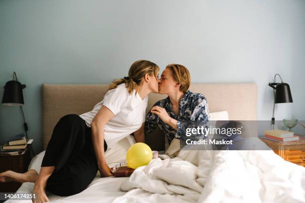 lesbian woman with birthday present kissing girlfriend on bed at home - beso en la boca fotografías e imágenes de stock