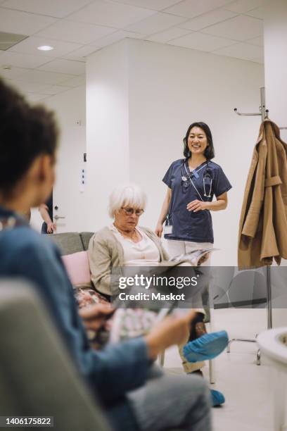 smiling female doctor looking at female patients sitting in waiting room at hospital - medical scrubs hanger stock pictures, royalty-free photos & images