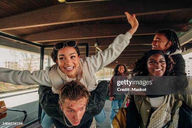 man and woman piggybacking happy friends at railroad station platform - gare ferroviaire photos et images de collection