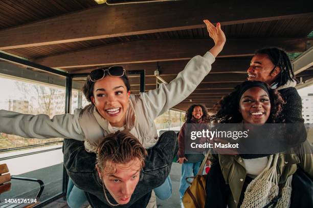 man and woman piggybacking happy friends at railroad station platform - happy friends stockfoto's en -beelden