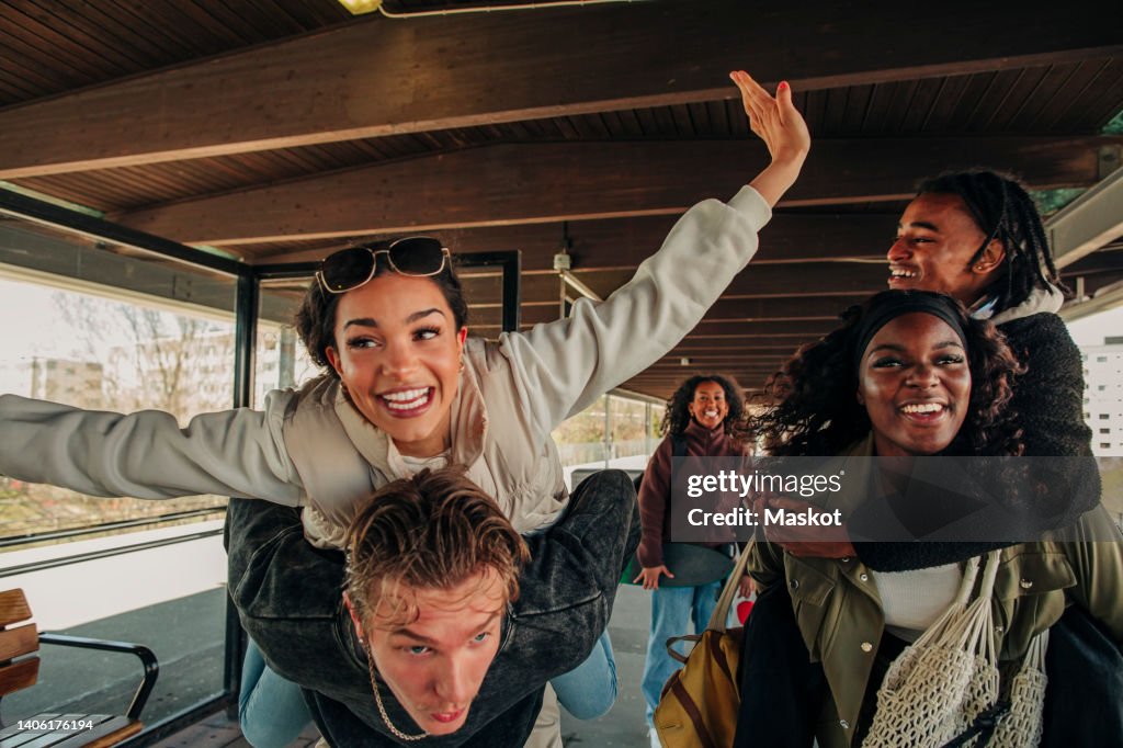 Man and woman piggybacking happy friends at railroad station platform