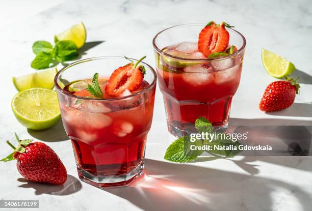 fresh summer strawberry, lime and mint cocktail with ice cubes. drinking glass of soda drink. cold lemonade recipe. two glasses of vitamin ready-to-eat mojito. closeup, horizontal, sunlight, white background - mojito stock pictures, royalty-free photos & images