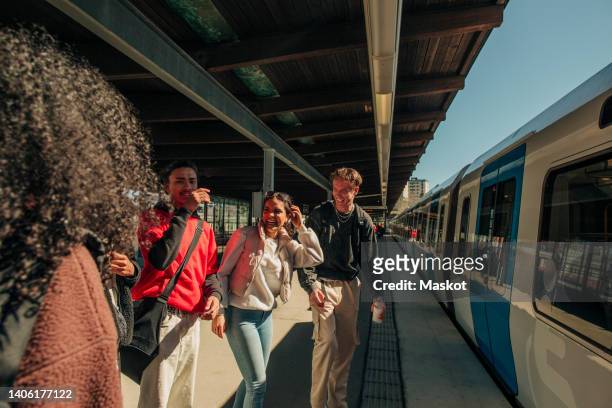 multiracial playful friends standing near train at railroad station - trein stockfoto's en -beelden