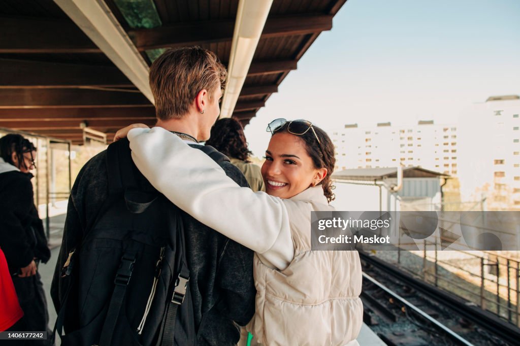 Portrait of smiling woman with arm around friend walking on railroad station