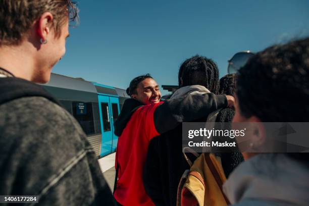 smiling man looking over shoulder with arm around friend at railroad station - train station stock-fotos und bilder