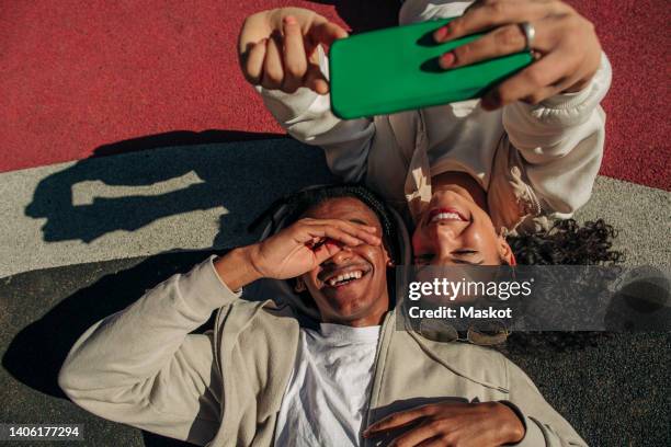 happy young friends taking selfie through smart phone while lying in playground - generation z friends stock pictures, royalty-free photos & images