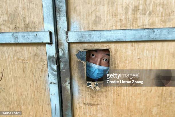 Resident looks through an hole in the fence from inside a locked down area on June 30, 2022 in Beijing, China. China is trying to contain a spike in...
