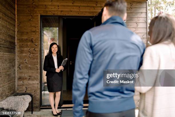 smiling real estate agent greeting couple at entrance of house - estate agent stock pictures, royalty-free photos & images