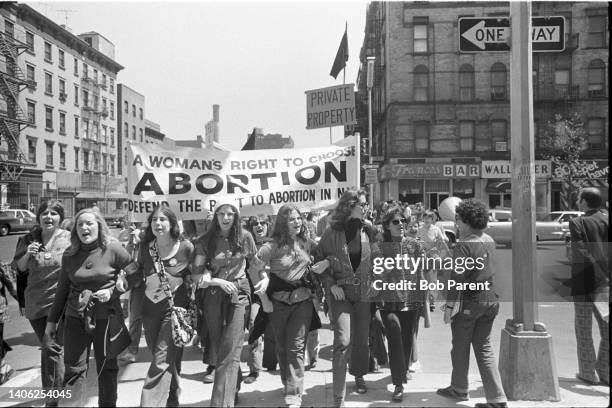 Women protesters hold up signs against state abortion regulations on May 6, 1972. One woman holds a megaphone as the women march arm in arm across...