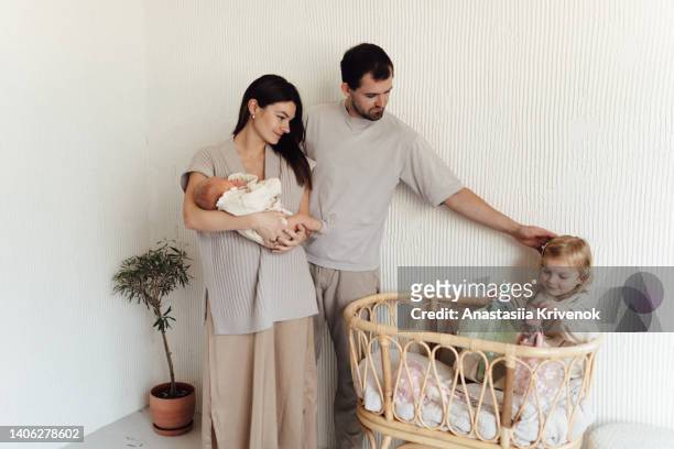 young mother, father with her 3 years old daughter putting a little newborn sister to sleep in her crib. - 30 34 years stock-fotos und bilder