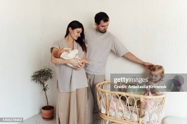 young mother, father with her 3 years old daughter putting a little newborn sister to sleep in her crib. - 30 39 years imagens e fotografias de stock