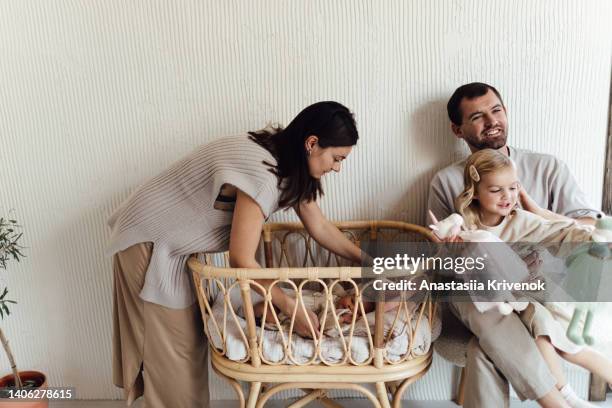 young mother, father with her 3 years old daughter putting a little newborn sister to sleep in her crib. - 30 39 years 個照片及圖片檔