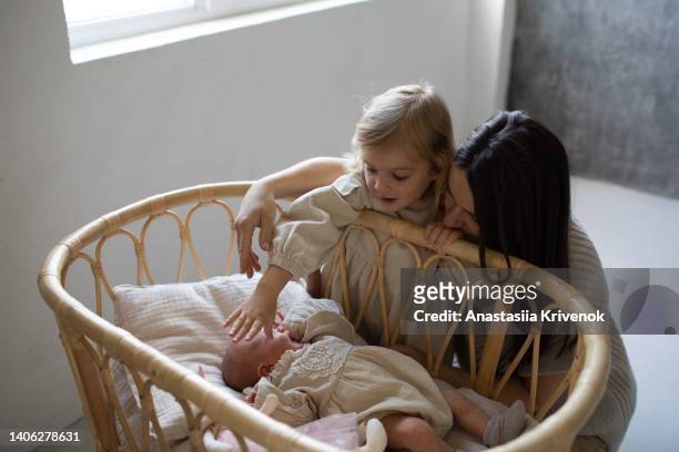 young mom with her 3 years old daughter putting a little newborn sister to sleep in her cribñ - 30 34 years stock-fotos und bilder