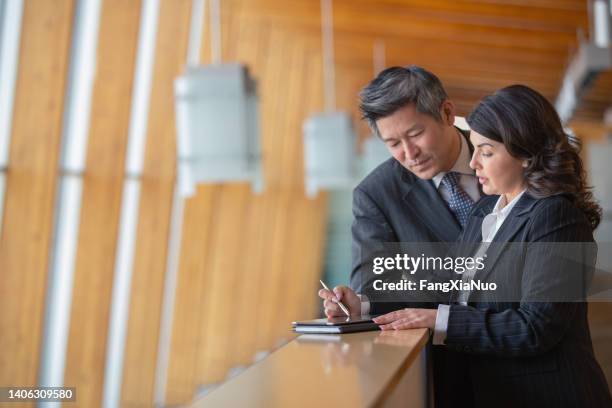 empresaria caucásica madura y hombre de negocios asiático chino de pie en el balcón de la oficina tomando notas - político fotografías e imágenes de stock