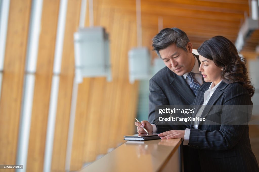 Mature Caucasian businesswoman and Chinese Asian businessman standing on office balcony taking notes