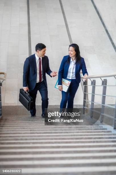 pacific islander ethnicity businessman with mature asian businesswoman with briefcase climbing a staircase in office lobby - canadian pacific women stock pictures, royalty-free photos & images