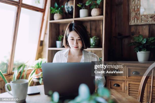 giovane freelance asiatico che lavora online sul computer portatile dall'ufficio di casa. imprenditrice, imprenditrice, blogger, libera professionista che lavora da casa in un'atmosfera accogliente. stile di vita e tecnologia - blog foto e immagini stock