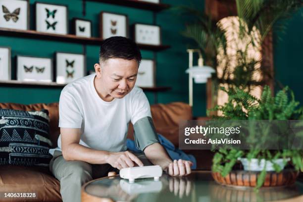 アジアの上級男性は、血圧モニターで腕の自宅で血圧をチェックしています。高齢者とヘルスケアの概念 - 心臓病 ストックフォトと画像