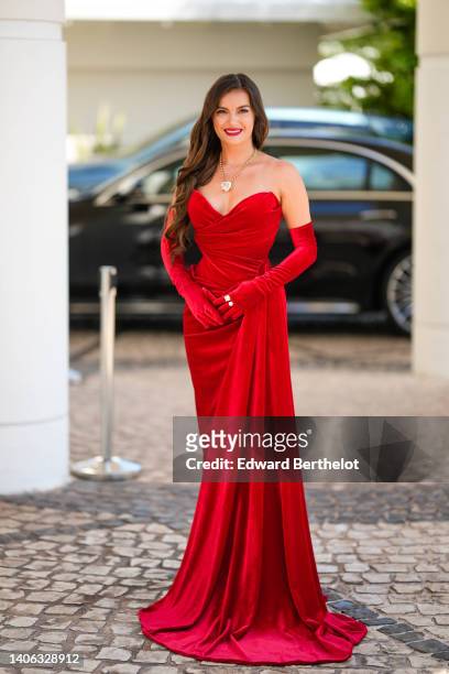 Guest wears a gold long necklace with a large diamond pendant in shape of heart, red velvet heart-neck / shoulder-off / long dress, matching red...