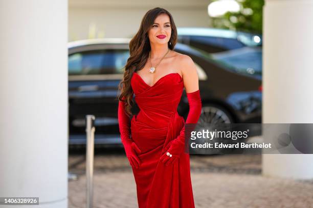 Guest wears a gold long necklace with a large diamond pendant in shape of heart, red velvet heart-neck / shoulder-off / long dress, matching red...