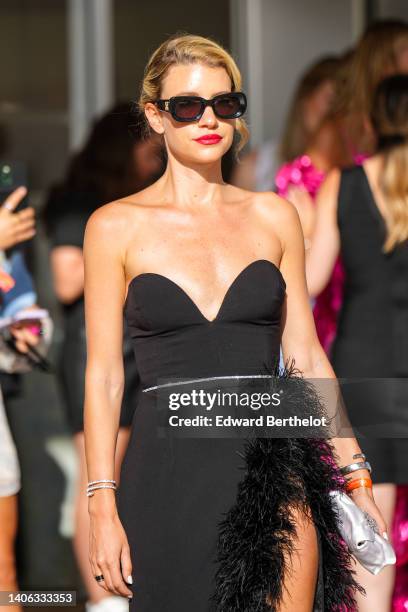 Guest wears black sunglasses from Off-White, a black heart-neck / shoulder-off / long slit dress with embroidered feathers borders, a silver watch...