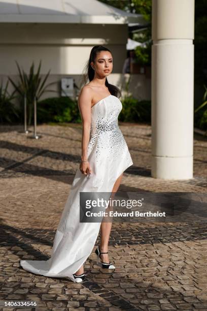 Guest wears silver earrings, a white asymmetric shoulder-off with embroidered mirror long asymmetric dress, a clutch, black and white shiny leather...