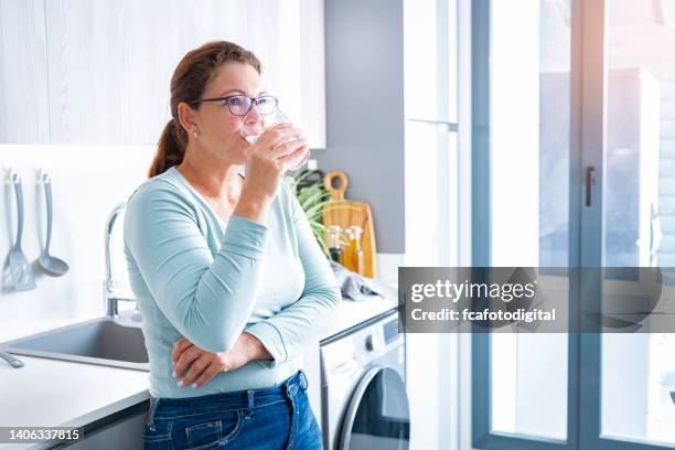 mature woman drinking water in modern kitchen - mature woman in water stock pictures, royalty-free photos & images