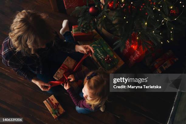 mom and her little daughter are unpacking christmas gifts. new year. new year's decor. casual style. mom and daughter with blond hair. christmas tree. - present unwrap stock-fotos und bilder