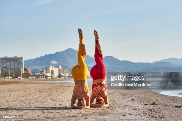 two women doing acroyoga in sirsasana position on the beach - shirshasana stock pictures, royalty-free photos & images