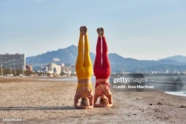 two women doing acroyoga in sirsasana position on the beach - shirshasana stock pictures, royalty-free photos & images