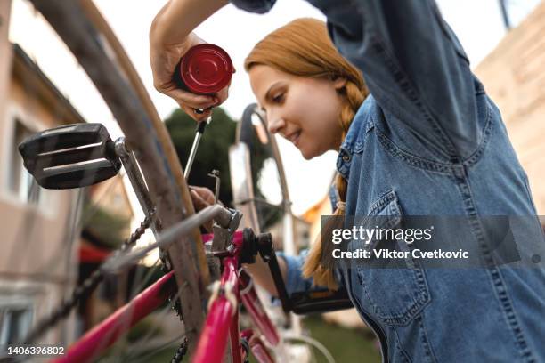 young woman repairing her old bicycle in back yard - adjusting stock pictures, royalty-free photos & images