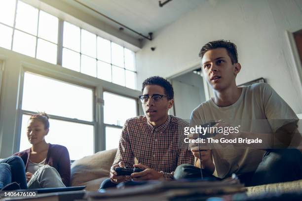 young men playing video game sitting by female friend in living room - console stock-fotos und bilder