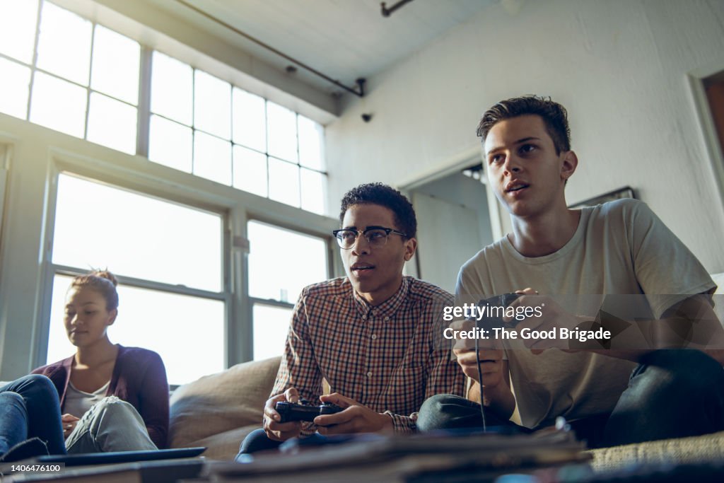 Young men playing video game sitting by female friend in living room