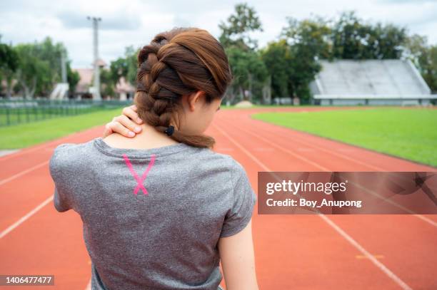 rear view of asian female runner having shoulder and neck pain after hard workout in stadium. - stijf stockfoto's en -beelden