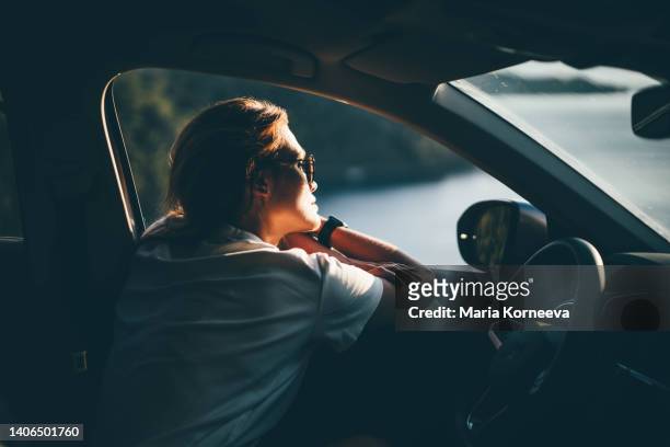 young woman enjoying the car ride at sunset. cute young woman hanging from a car. - driving photos et images de collection