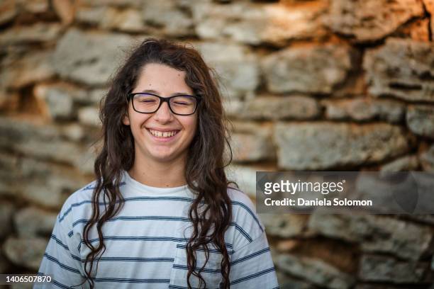 close up of teenager boy with long hair and eyeglasses near stone wall - boy with long hair stock pictures, royalty-free photos & images