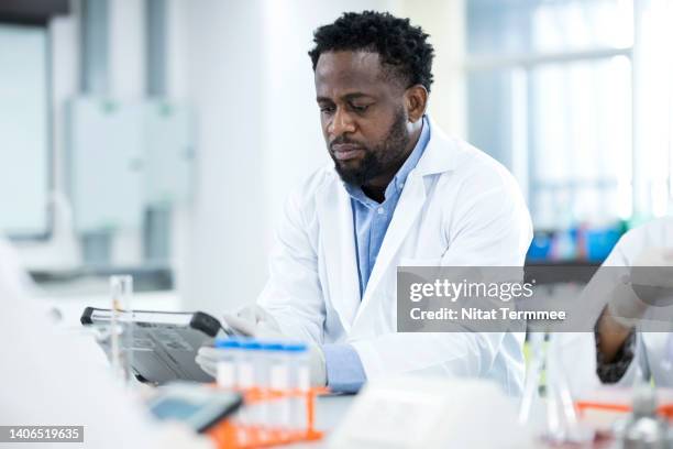 information for research and development of product development and commercialization in pharmaceutical industry. african american scientist working in a medical laboratory while using a digital tablet to  access research database. - genomics stock pictures, royalty-free photos & images