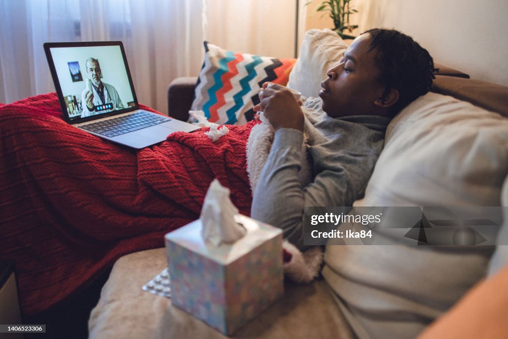 Junger kranker afroamerikanischer Mann, der über einen Laptop mit dem Arzt interagiert
