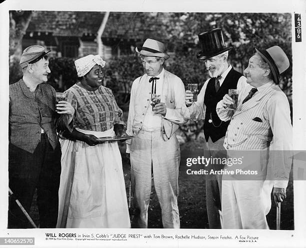 Will Rogers and others holding glasses of ice tea in a scene from the film 'Judge Priest', 1934.